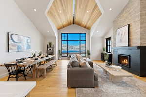Living room with a lit fireplace, light wood-type flooring, a high ceiling, and recessed lighting
