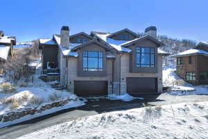View of front of house featuring a chimney, an attached garage, stone siding, and driveway