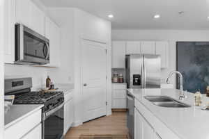 Kitchen featuring stainless steel appliances, white cabinetry, light wood-style flooring, light stone countertops, and recessed lighting