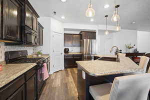Kitchen with a kitchen bar, black appliances, an island with sink, dark wood finish cabinets, and dark wood-style flooring