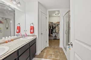 Full bathroom featuring double vanity, a walk in closet, a stall shower, and light stone finish flooring