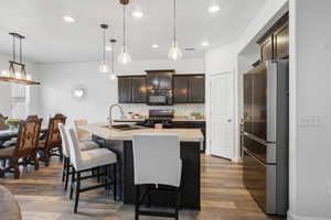 Kitchen featuring black appliances, dark wood finish cabinetry, dark wood-style flooring, and a center island with sink