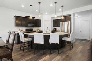 Kitchen with an island with sink, decorative light fixtures, black appliances, and dark wood-style flooring