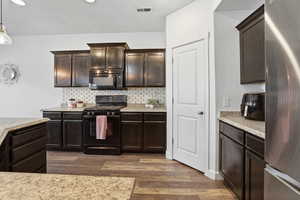 Kitchen featuring black appliances, dark wood finish cabinetry, dark wood finished floors, decorative backsplash, and light stone counters