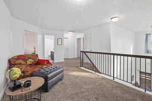 Living area featuring carpet, an upstairs landing, and a textured ceiling