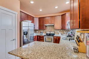 Kitchen with stainless steel appliances, light stone counters, a peninsula, decorative backsplash, and recessed lighting