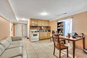 Kitchen featuring white range with electric stovetop, backsplash, light wood finish cabinets, light tile patterned floors, and light countertops
