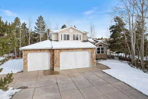 View of front of property with stone siding, concrete driveway, an attached garage, and stucco siding
