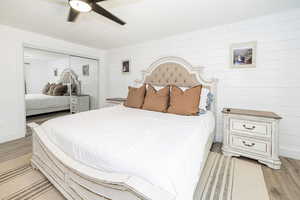 Bedroom featuring light wood finished floors, a ceiling fan, a closet, and wooden walls
