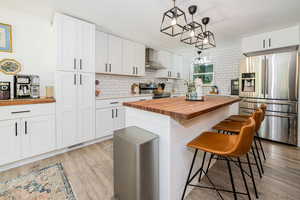 Kitchen with butcher block counters, stainless steel appliances, white cabinetry, and light wood-style floors