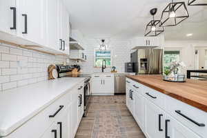 Kitchen with wood counters, white cabinetry, stainless steel appliances, hanging light fixtures, and light wood-style floors