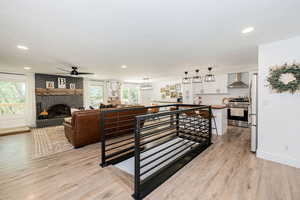Living room with a fireplace, light wood-style flooring, ceiling fan, and recessed lighting
