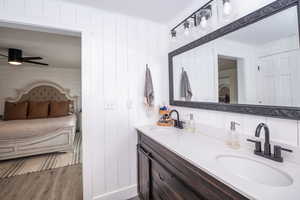 Full bathroom with double vanity, ensuite bathroom, ceiling fan, light wood finished floors, and wooden walls