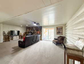 Living room featuring log walls, light colored carpet, and ceiling fan