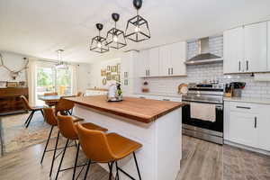 Kitchen with stainless steel range with electric cooktop, wood counters, pendant lighting, and a center island