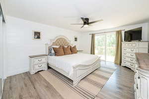 Bedroom featuring ceiling fan, access to exterior, light wood-type flooring, and wood walls