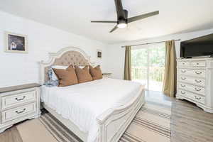 Bedroom with a ceiling fan, access to exterior, wood walls, and light wood-style flooring