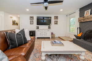 Living area with a fireplace, light wood-type flooring, wooden walls, a ceiling fan, and ornamental molding