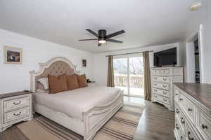 Bedroom with a ceiling fan, dark wood-type flooring, access to outside, wooden walls, and a textured ceiling