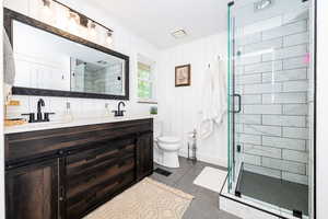 Bathroom with double vanity, a shower stall, and wooden walls
