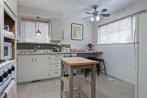 Kitchen with stainless steel appliances, white cabinetry, a ceiling fan, light tile patterned floors, and tasteful backsplash
