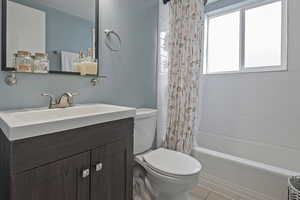 Full bath with vanity, shower / bath combo with shower curtain, and light tile patterned floors