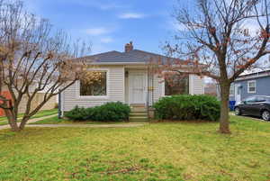 View of front of property featuring a chimney, a front yard, and a shingled roof