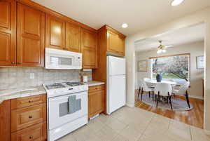 Kitchen with white appliances, wood finish cabinetry, light tile patterned floors, decorative backsplash, and a ceiling fan