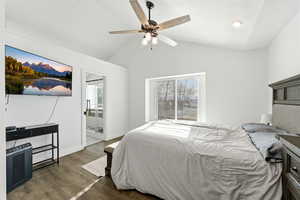 Bedroom with vaulted ceiling, multiple windows, dark wood-style flooring, a ceiling fan, and ensuite bathroom