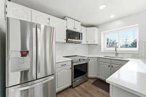 Kitchen with stainless steel appliances, white cabinetry, dark wood-style flooring, recessed lighting, and backsplash