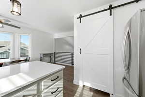 Kitchen featuring freestanding refrigerator, a barn door, white cabinetry, light countertops, and dark wood-style flooring