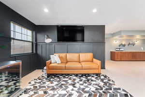 Living room with a decorative wall, light colored carpet, and recessed lighting