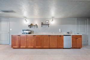 Kitchen with a textured ceiling, light carpet, wood finish cabinetry, dishwasher, and open shelves