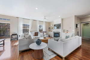 Living room with dark wood finished floors, a ceiling fan, a glass covered fireplace, and recessed lighting