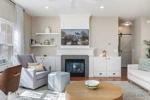 Living room with a barn door, a fireplace, ceiling fan, wood finished floors, and recessed lighting