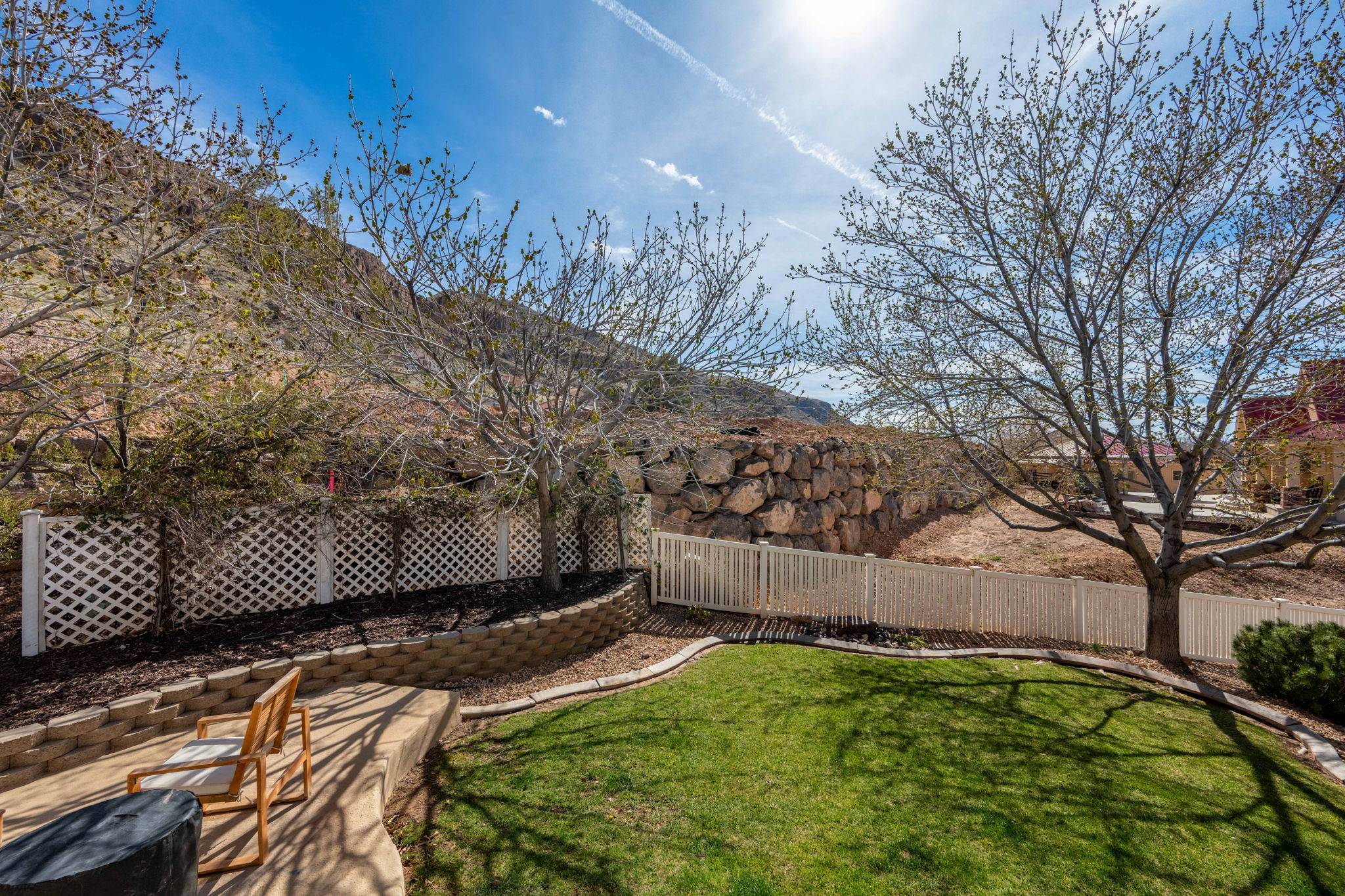 Tiered backyard featuring a manicured lawn, concrete patio, and white lattice fencing