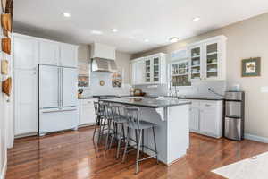 Kitchen with a breakfast bar area, glass insert cabinets, freestanding refrigerator, white cabinets, and recessed lighting