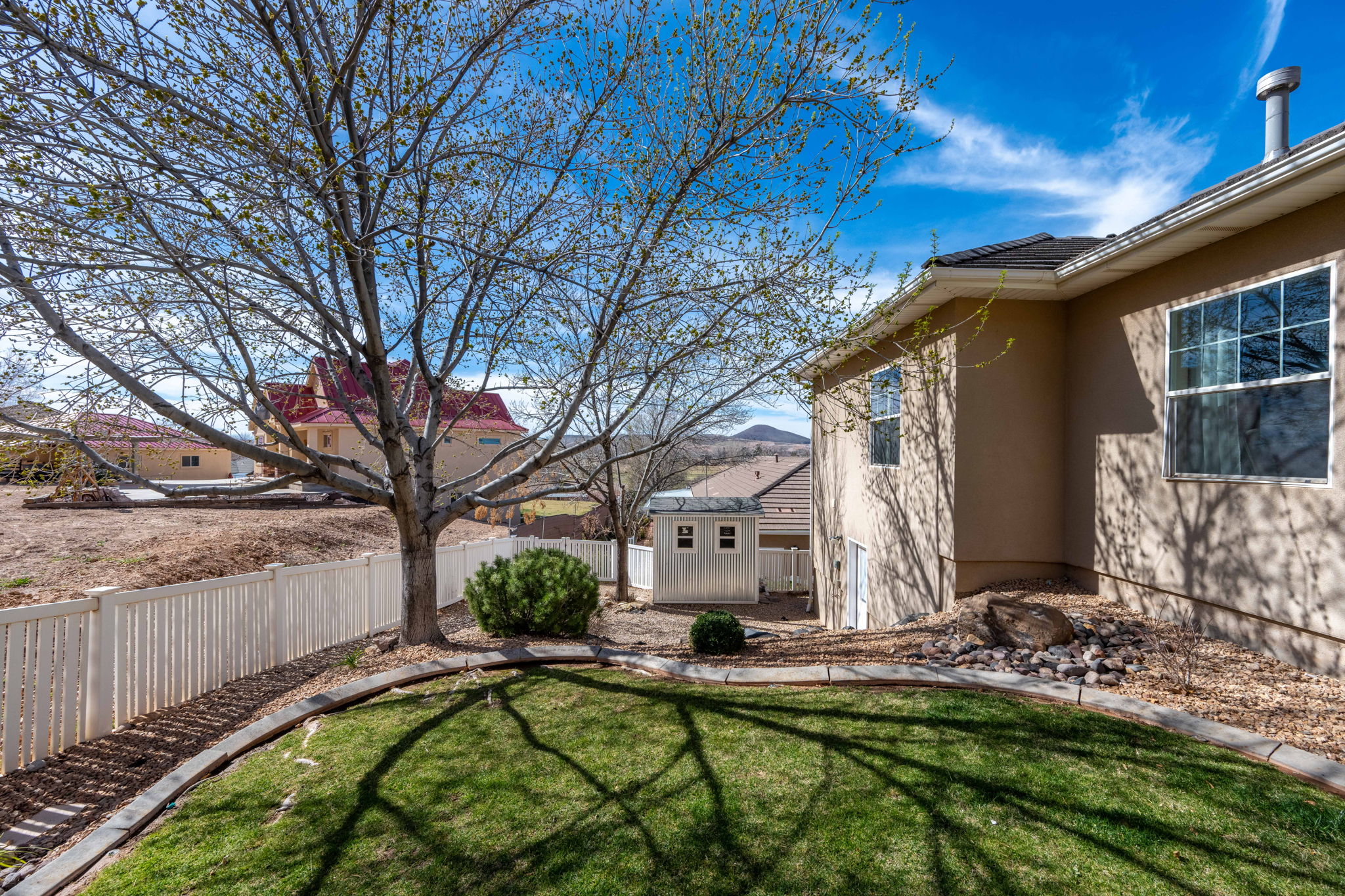 Expansive backyard featuring a manicured lawn, established tree, white picket fencing, and a detached storage shed