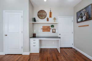 Unfurnished office with built in study area and dark wood-style flooring