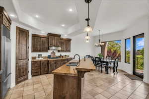 Kitchen featuring dark wood finish cabinetry, a tray ceiling, built in fridge, an island with sink, and a breakfast bar area