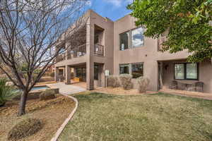 Rear view of house featuring a balcony, stucco siding, a patio area, a lawn, and an outdoor pool