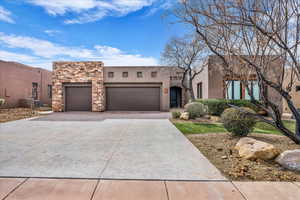 Southwest-style home featuring an attached garage, driveway, stucco siding, and stone siding