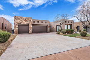 Pueblo revival-style home with a garage, concrete driveway, stucco siding, and stone siding