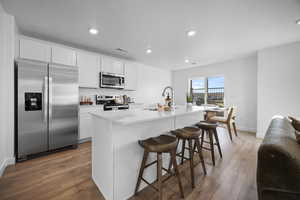 Kitchen featuring stainless steel appliances, a breakfast bar area, an island with sink, white cabinets, and recessed lighting