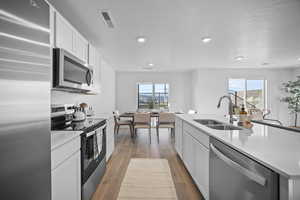 Kitchen featuring stainless steel appliances, white cabinetry, dark wood finished floors, a kitchen island with sink, and plenty of natural light