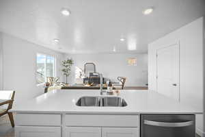 Kitchen with dishwasher, white cabinetry, open floor plan, light stone counters, and an island with sink