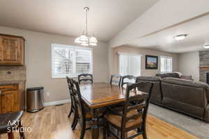 Dining area with vaulted ceiling, light wood-style flooring, suspended lighting, and a stone fireplace