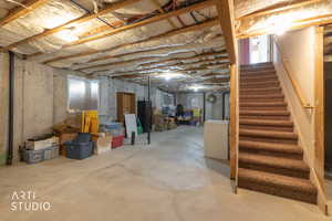 Unfinished basement with stairs and white refrigerator