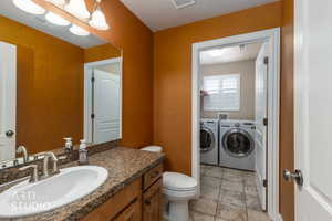 Half bath featuring vanity, independent washer and dryer, and light tile floor.