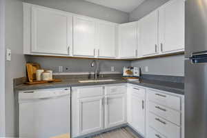 Kitchen with dark countertops, dishwasher, freestanding refrigerator, and white cabinetry